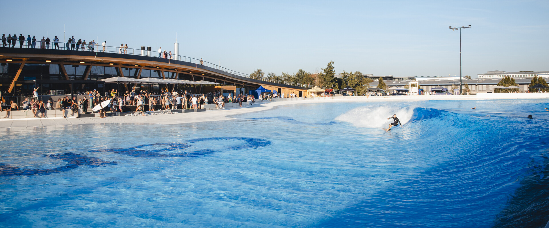 Surfer:innen im Wavepool des Surfparks bei M&uuml;nchen, die gemeinsam perfekte Wellen reiten &ndash; Surfen f&uuml;r alle Levels.