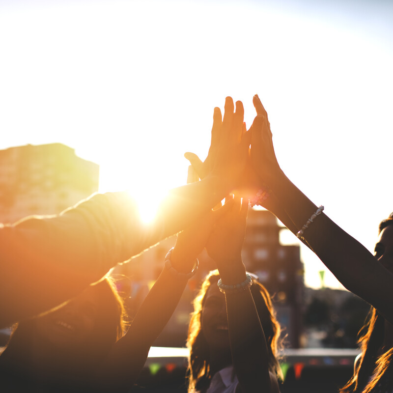Vier lachende Menschen klatschen sich ab in Abendstimmung